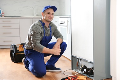 Male technician with tools near broken refrigerator indoors