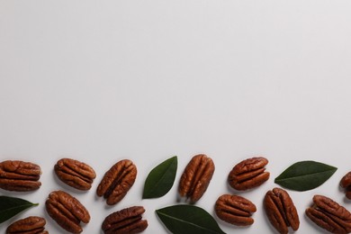 Photo of Delicious pecan nuts and green leaves on white background, flat lay. Space for text