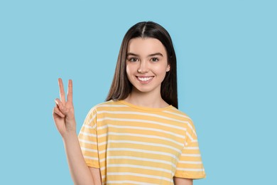 Teenage girl showing peace sign on light blue background