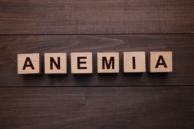 Photo of Word Anemia made with cubes on wooden table, flat lay