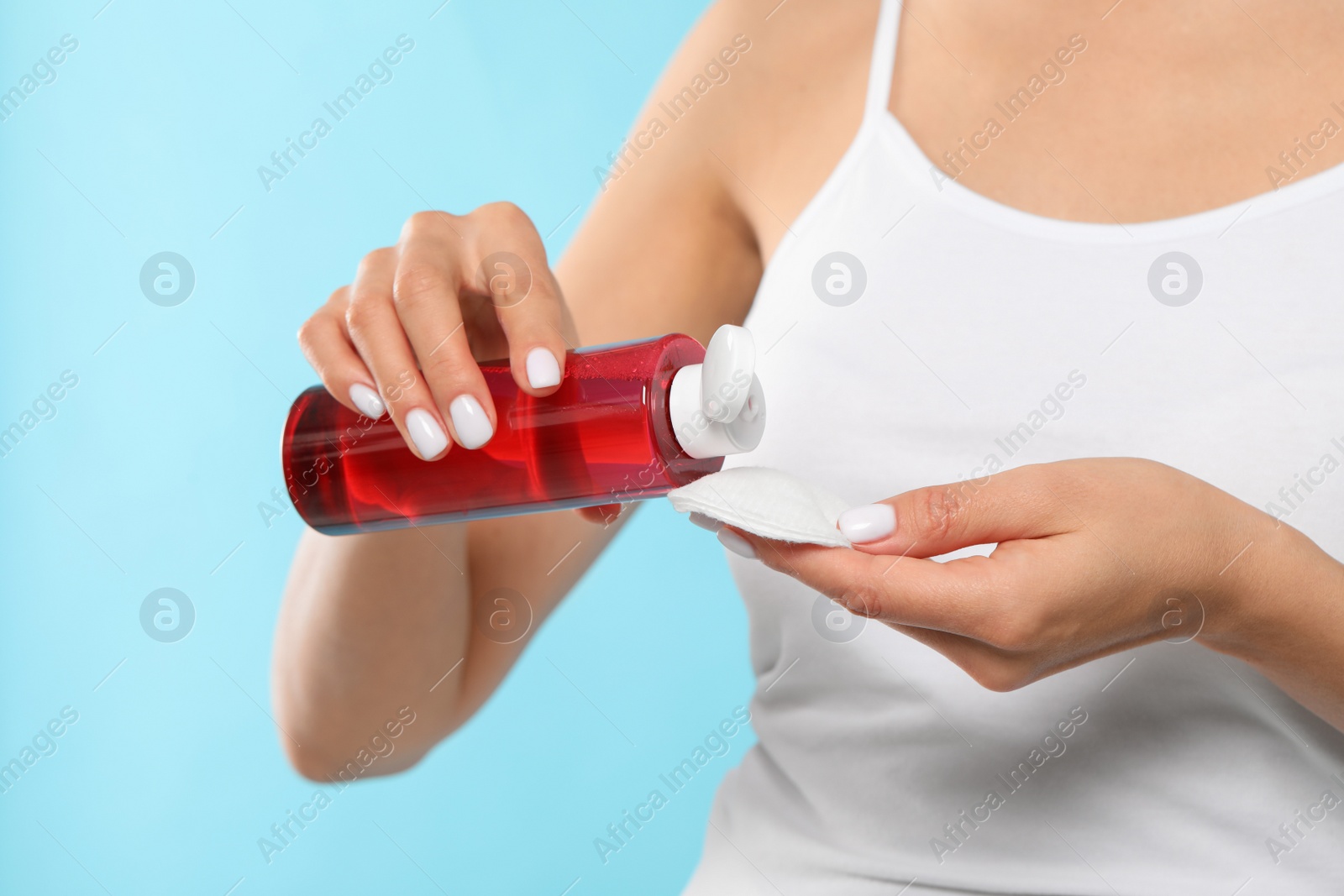 Photo of Woman pouring micellar water onto cotton pad on light blue background, closeup