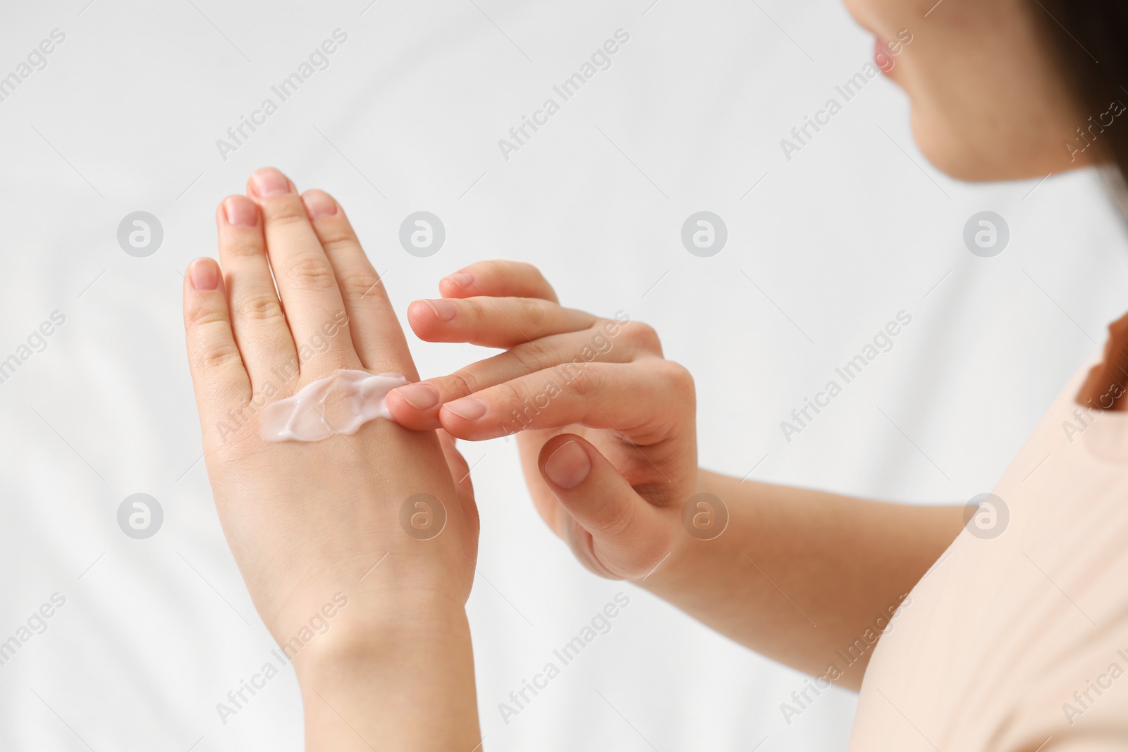 Photo of Young woman with dry skin applying cream onto her hand on bed, closeup