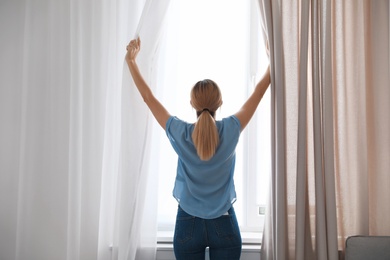 Photo of Woman opening curtains and looking out of window at home