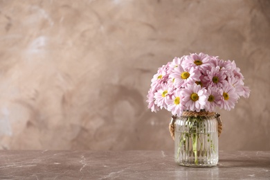 Photo of Vase with beautiful chamomile flowers on table against color background. Space for text