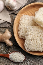 Photo of Bowl with dried rice noodles and ingredients on wooden table, flat lay