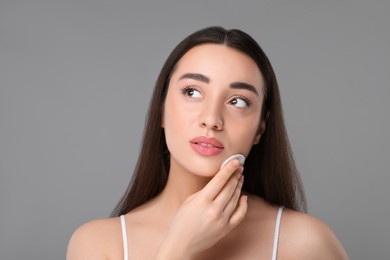 Beautiful woman removing makeup with cotton pad on gray background