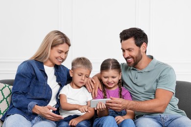 Photo of Happy family with smartphone spending time together on sofa at home