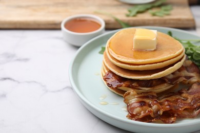 Tasty pancakes with butter, fried bacon and fresh arugula on white marble table, closeup. Space for text