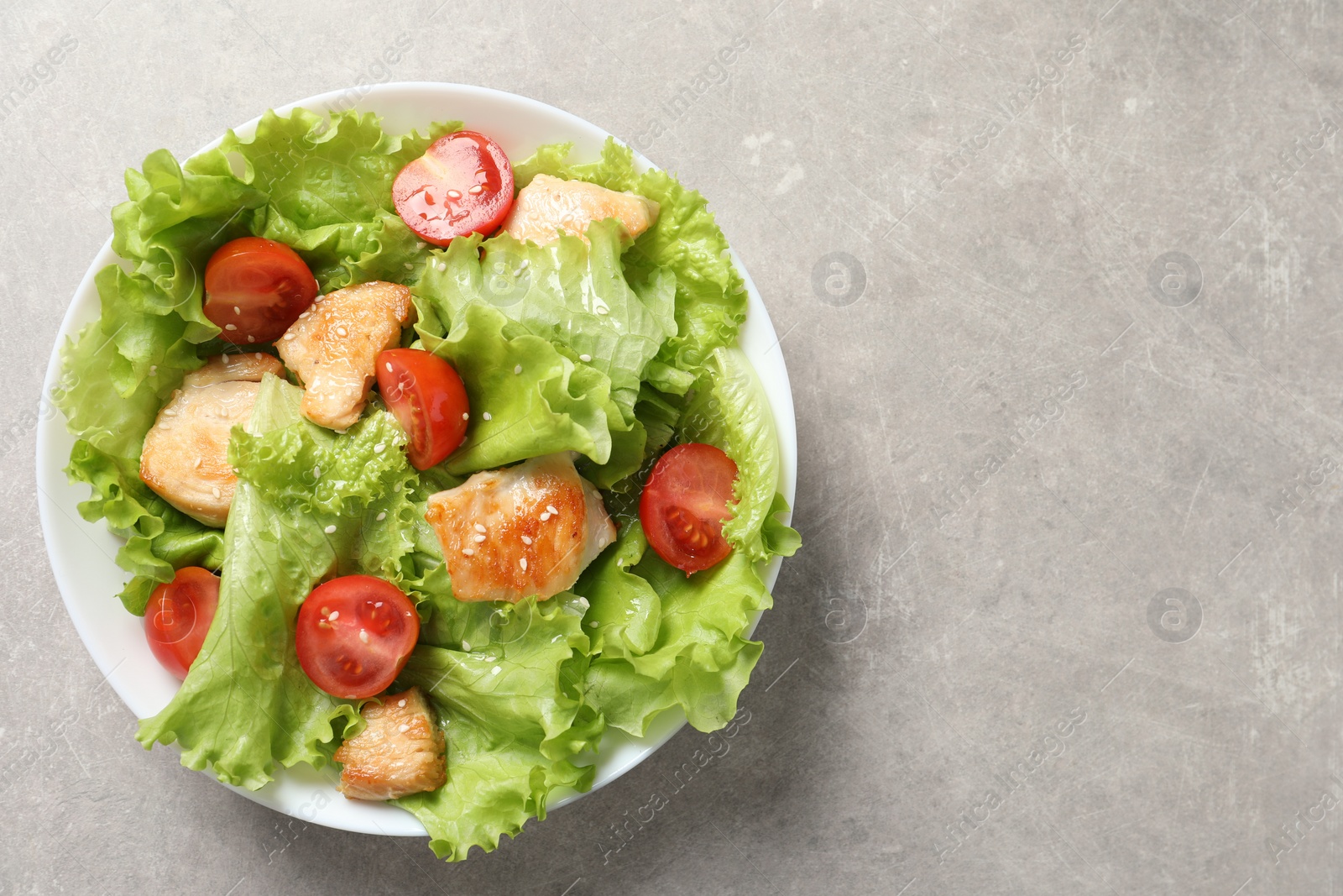 Photo of Delicious salad with chicken and cherry tomato on light grey table, top view. Space for text