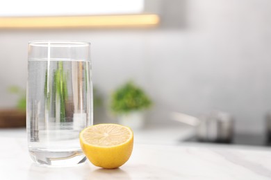 Photo of Glass with clear water and half of lemon on white table in kitchen, space for text