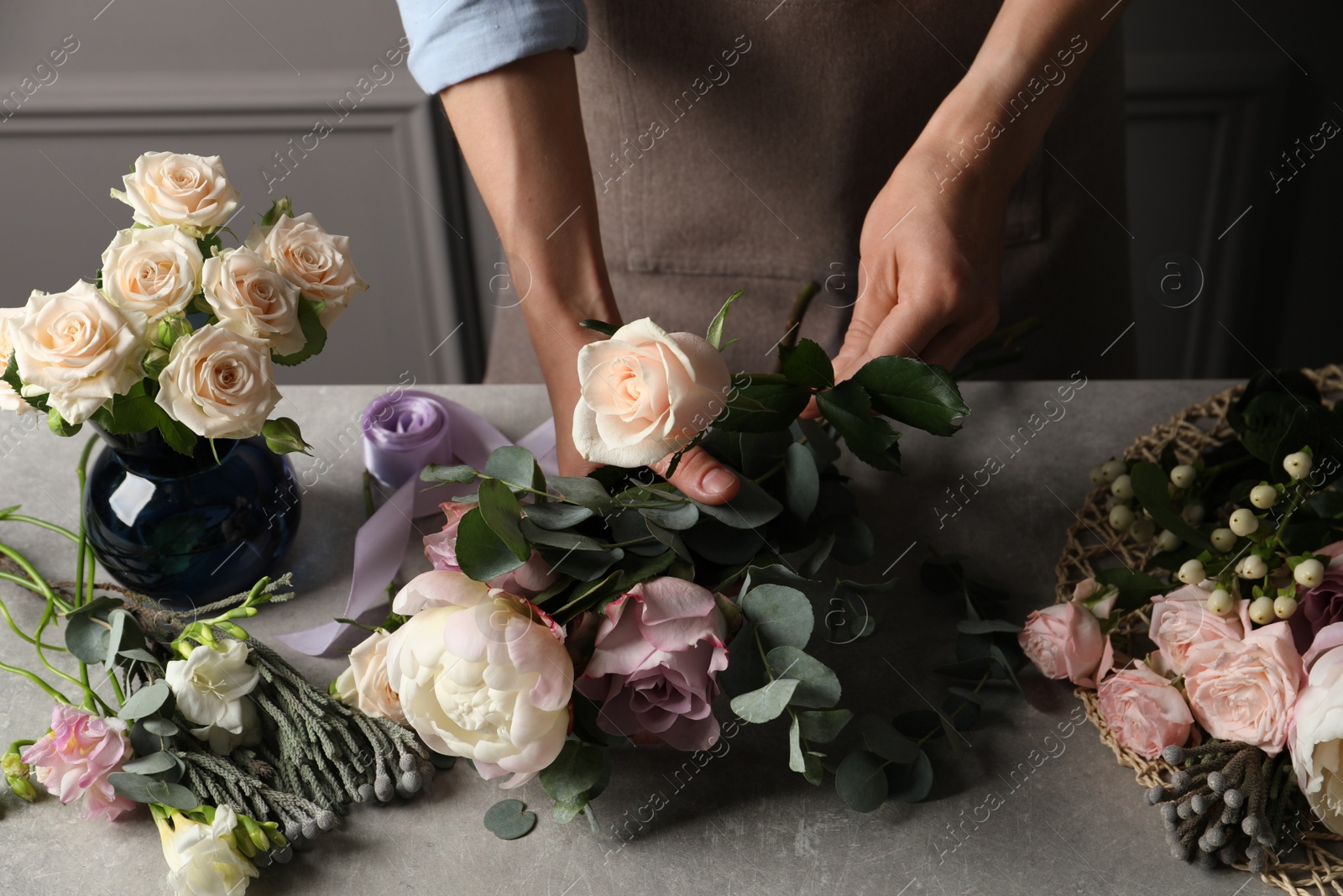 Photo of Florist creating beautiful bouquet at light grey table indoors, closeup