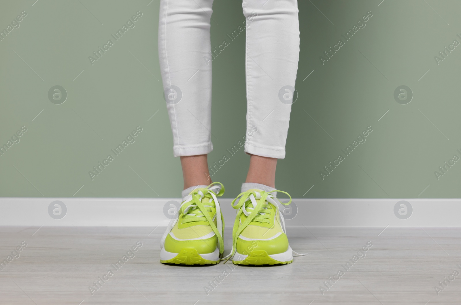 Photo of Woman wearing pair of new stylish sneakers near light green wall, closeup