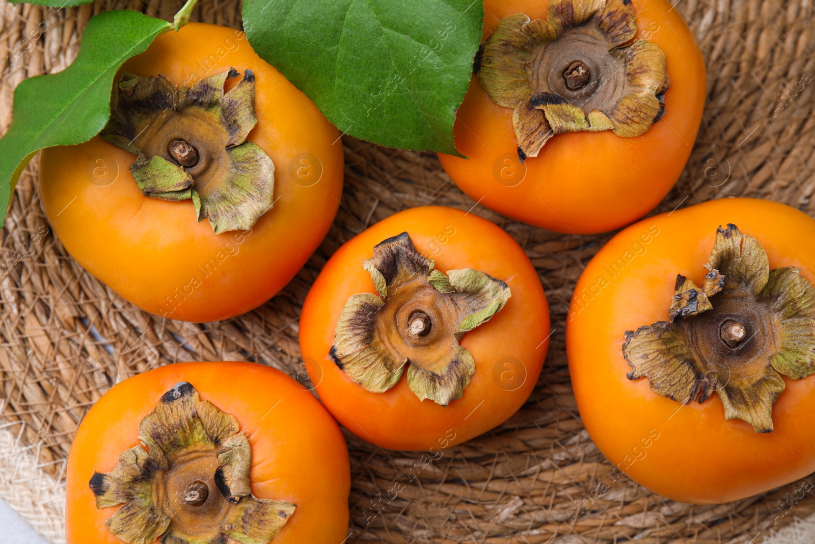Photo of Delicious ripe juicy persimmons on wicker mat, flat lay