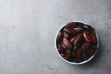 Photo of Bowl of sweet dates on grey background, top view with space for text. Dried fruit as healthy snack