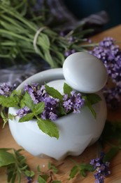 Mortar with fresh lavender flowers, mint and pestle on table, closeup