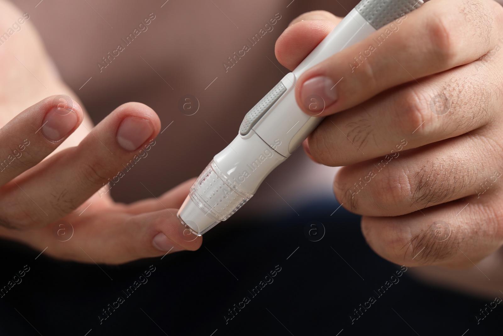 Photo of Diabetes test. Man checking blood sugar level with lancet pen on blurred background, closeup