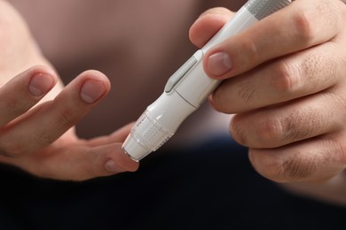 Diabetes test. Man checking blood sugar level with lancet pen on blurred background, closeup