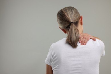 Photo of Mature woman suffering from pain in her neck on grey background, back view. Space for text