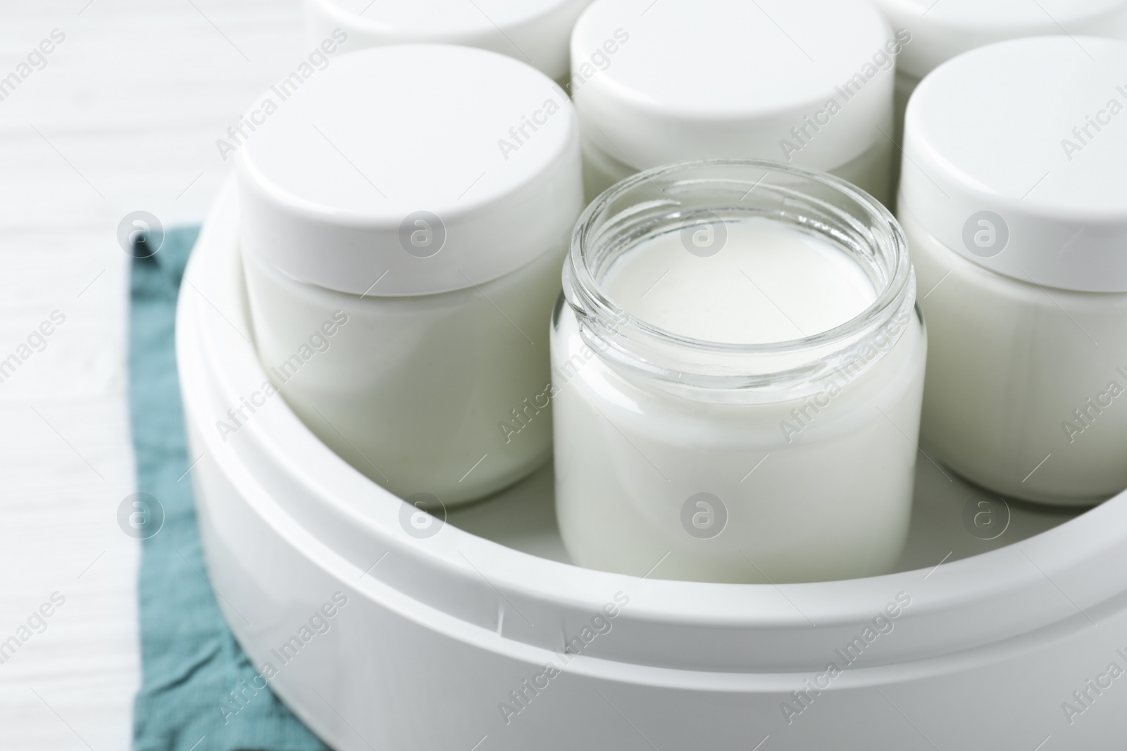 Photo of Modern yogurt maker with full jars on white wooden table, closeup