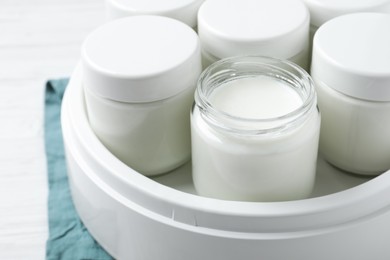 Modern yogurt maker with full jars on white wooden table, closeup