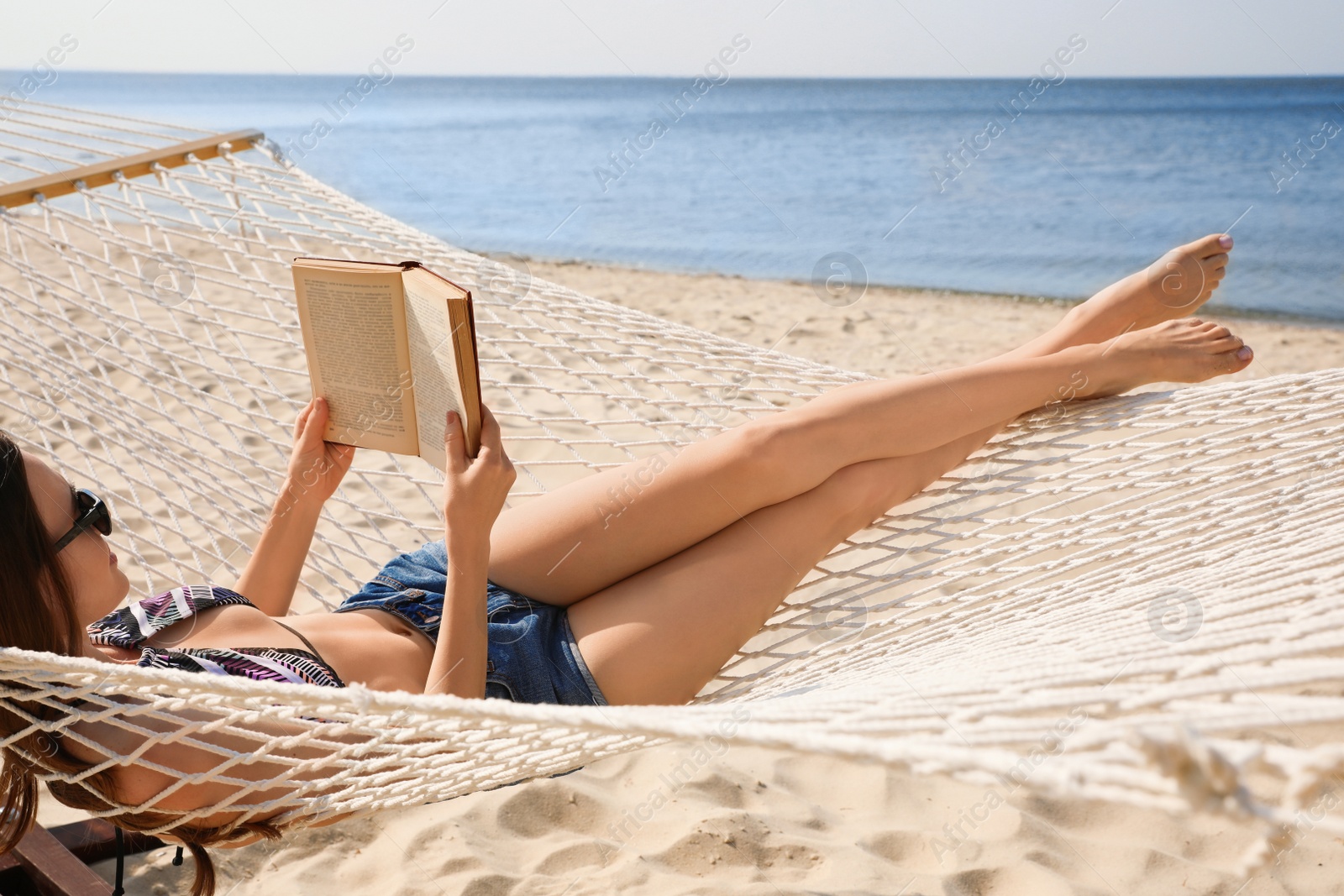 Photo of Young woman reading book in hammock on beach