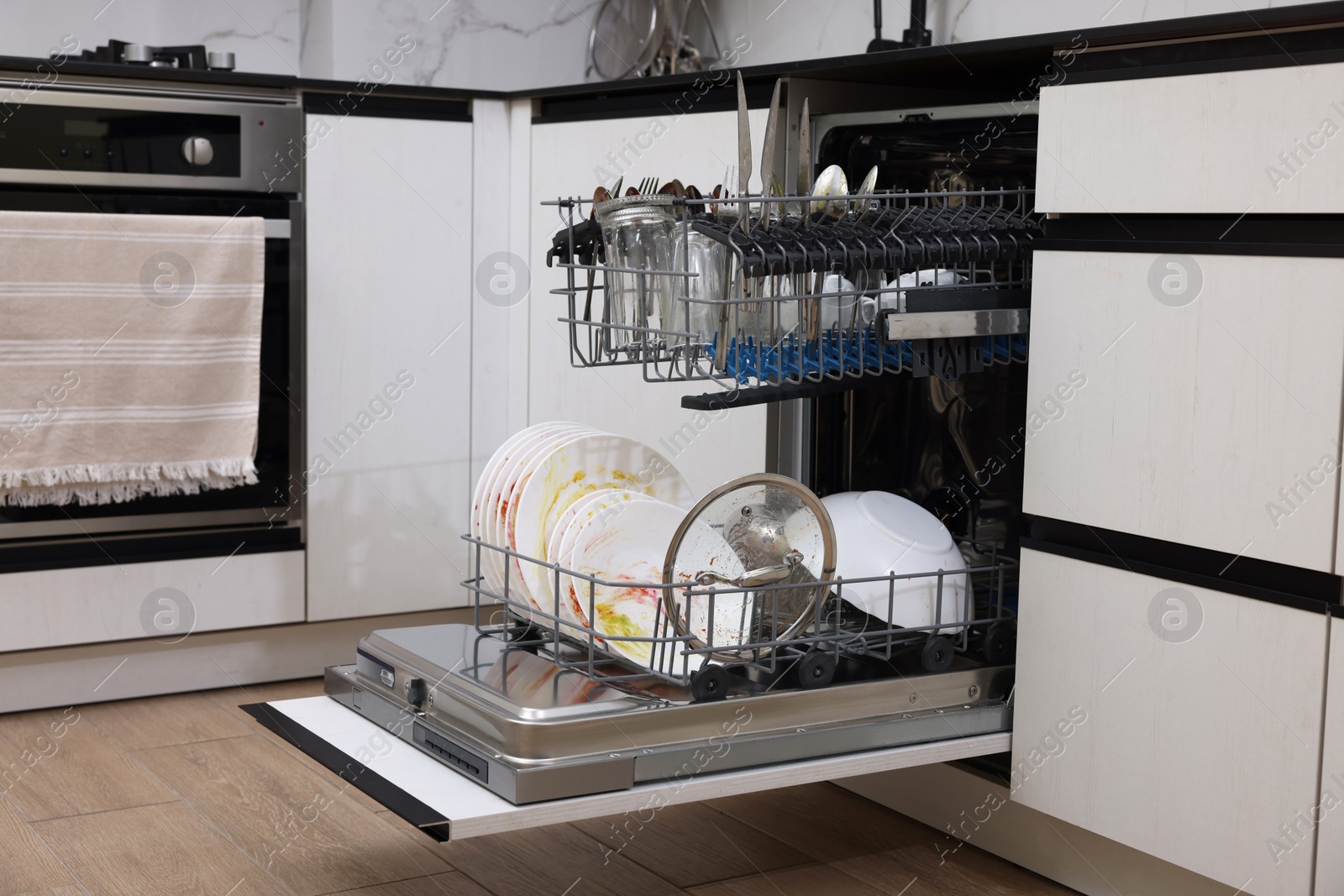 Photo of Open modern dishwasher with dirty tableware in kitchen