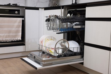 Photo of Open modern dishwasher with dirty tableware in kitchen