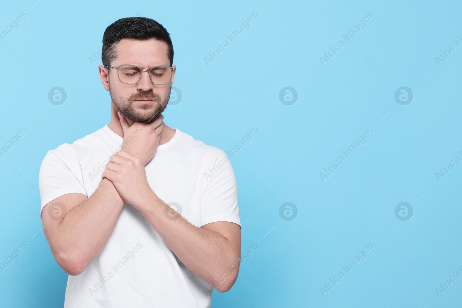 Photo of Man suffering from sore throat on light blue background, space for text