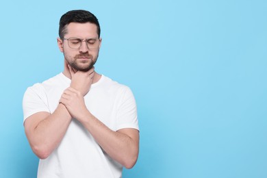 Photo of Man suffering from sore throat on light blue background, space for text