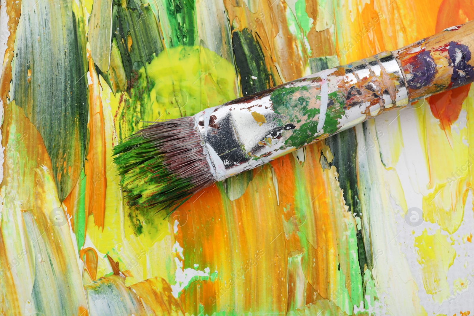 Photo of Paintbrush and strokes of colorful oil paints on canvas, top view