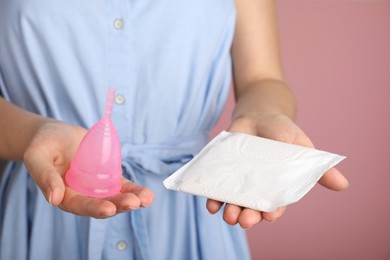Photo of Woman holding menstrual cup and disposable pad on pink background, closeup