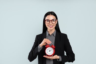 Photo of Businesswoman holding alarm clock on light grey  background. Time management