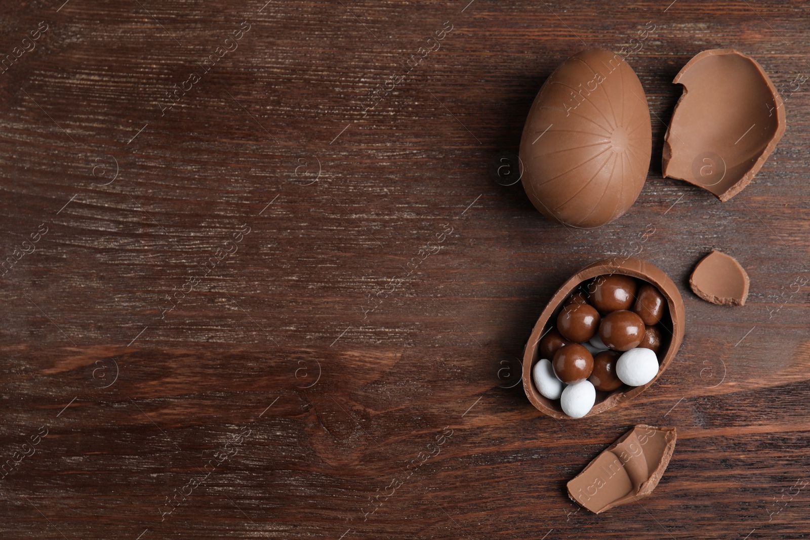 Photo of Whole and broken chocolate eggs with candies on wooden table, flat lay. Space for text