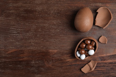 Whole and broken chocolate eggs with candies on wooden table, flat lay. Space for text