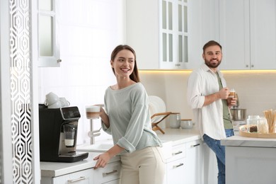 Beautiful young woman using modern coffee machine in kitchen