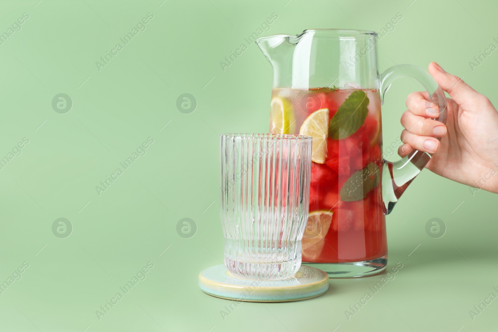 Photo of Woman holding jug of tasty watermelon drink with lime on pale light green background, closeup. Space for text