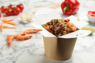 Photo of Box of wok noodles with seafood on white marble table, closeup