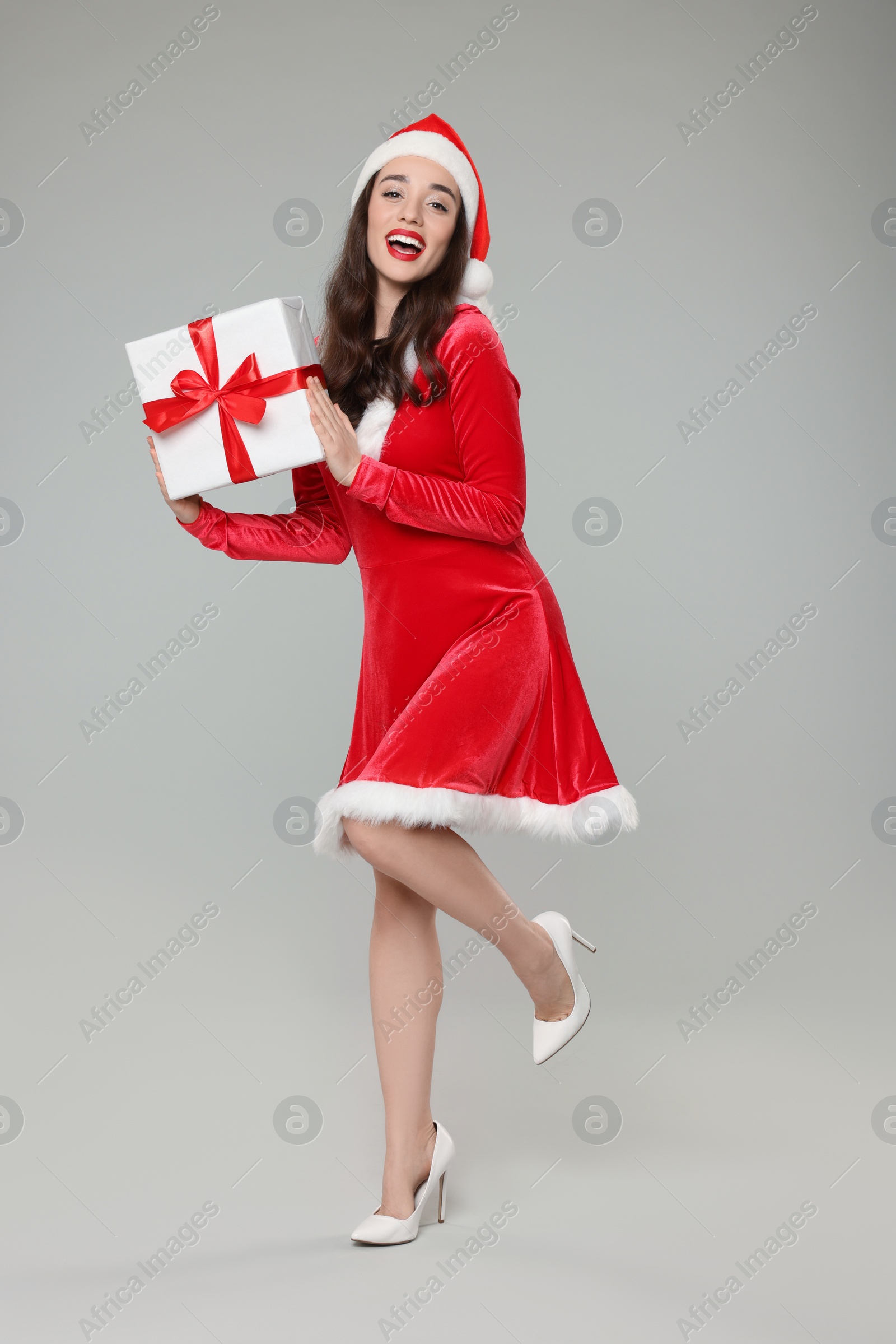 Photo of Beautiful young woman in red dress and Santa hat with Christmas gift on grey background