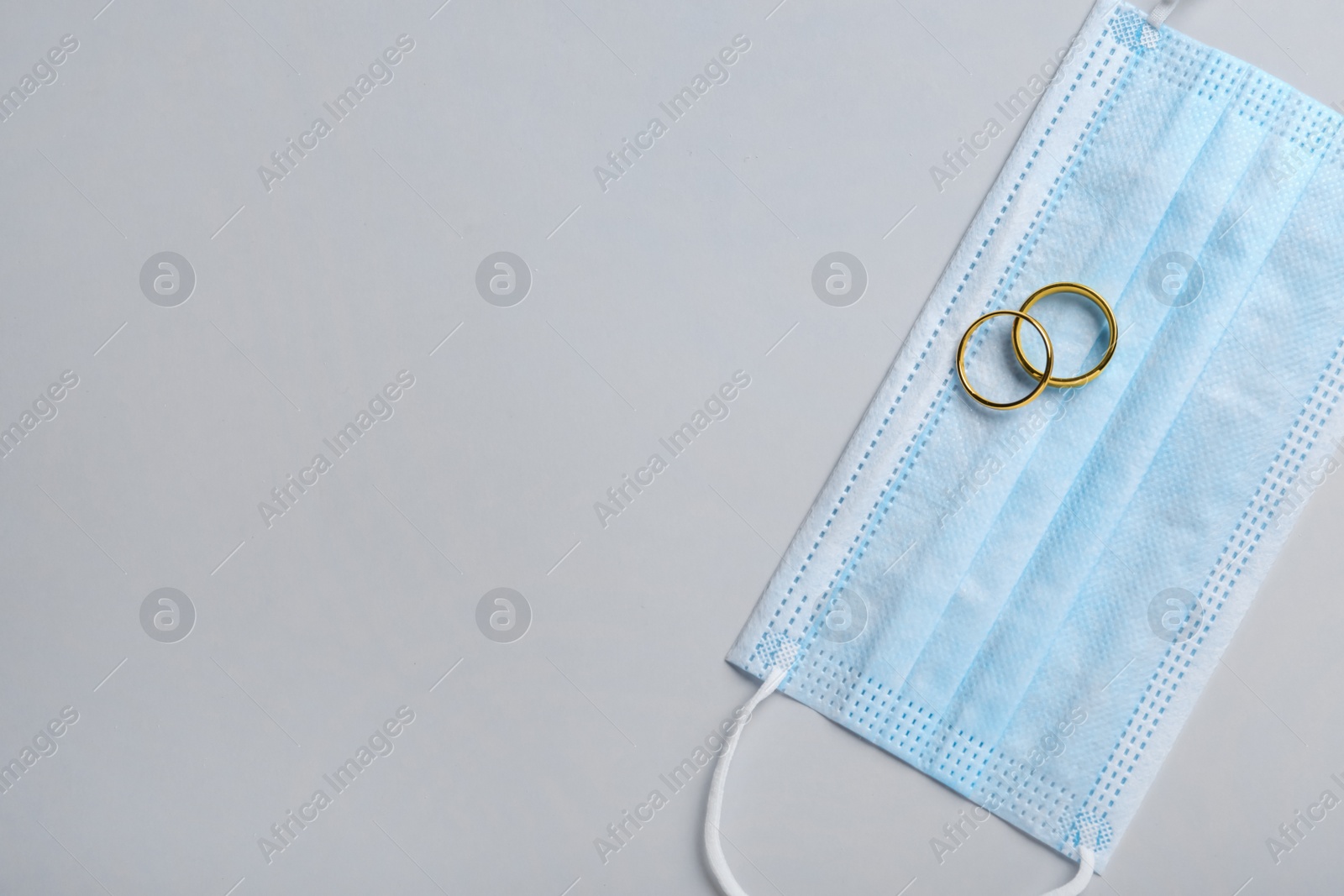 Photo of Wedding rings and medical mask on grey background, top view with space for text. Divorce during coronavirus outbreak