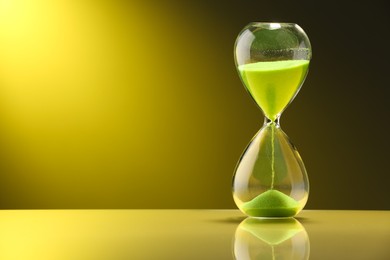 Photo of Hourglass with light green flowing sand on table against color background. Space for text