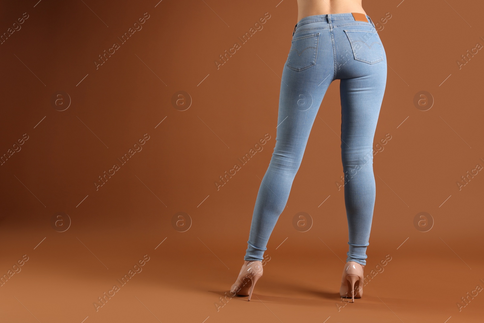 Photo of Woman wearing stylish light blue jeans and high heels shoes on brown background, closeup. Space for text