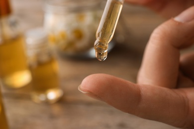 Photo of Woman applying essential oil on finger over table, closeup. Space for text