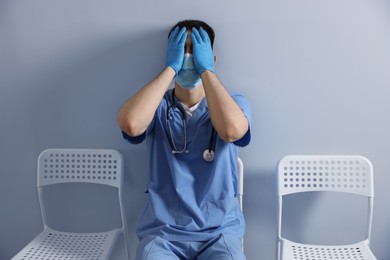 Photo of Exhausted doctor sitting on chair near grey wall in hospital