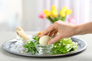 Photo of Woman holding traditional egg over Passover (Pesach) Seder plate on table, closeup. Space for text