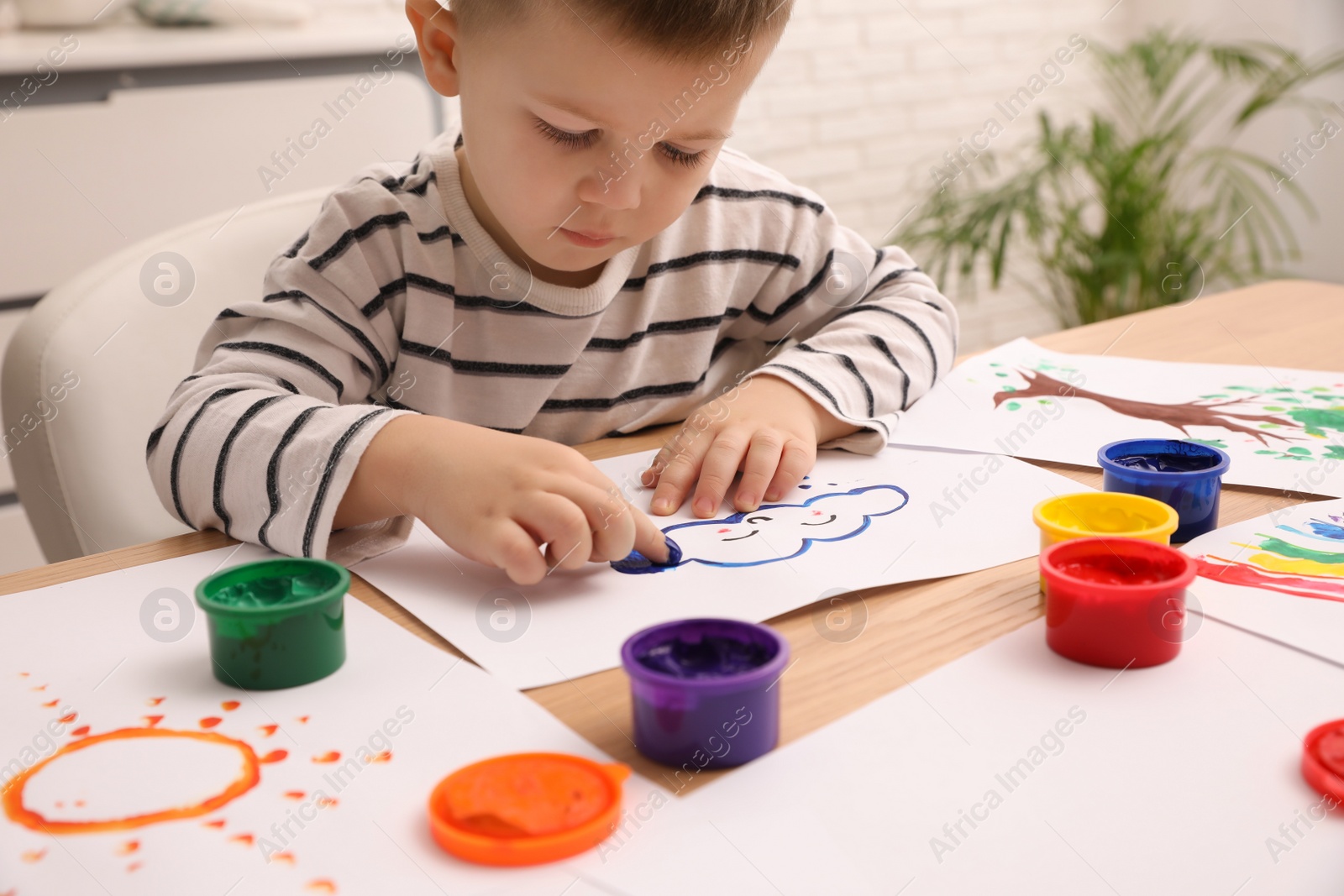 Photo of Little boy painting with finger at wooden table in room