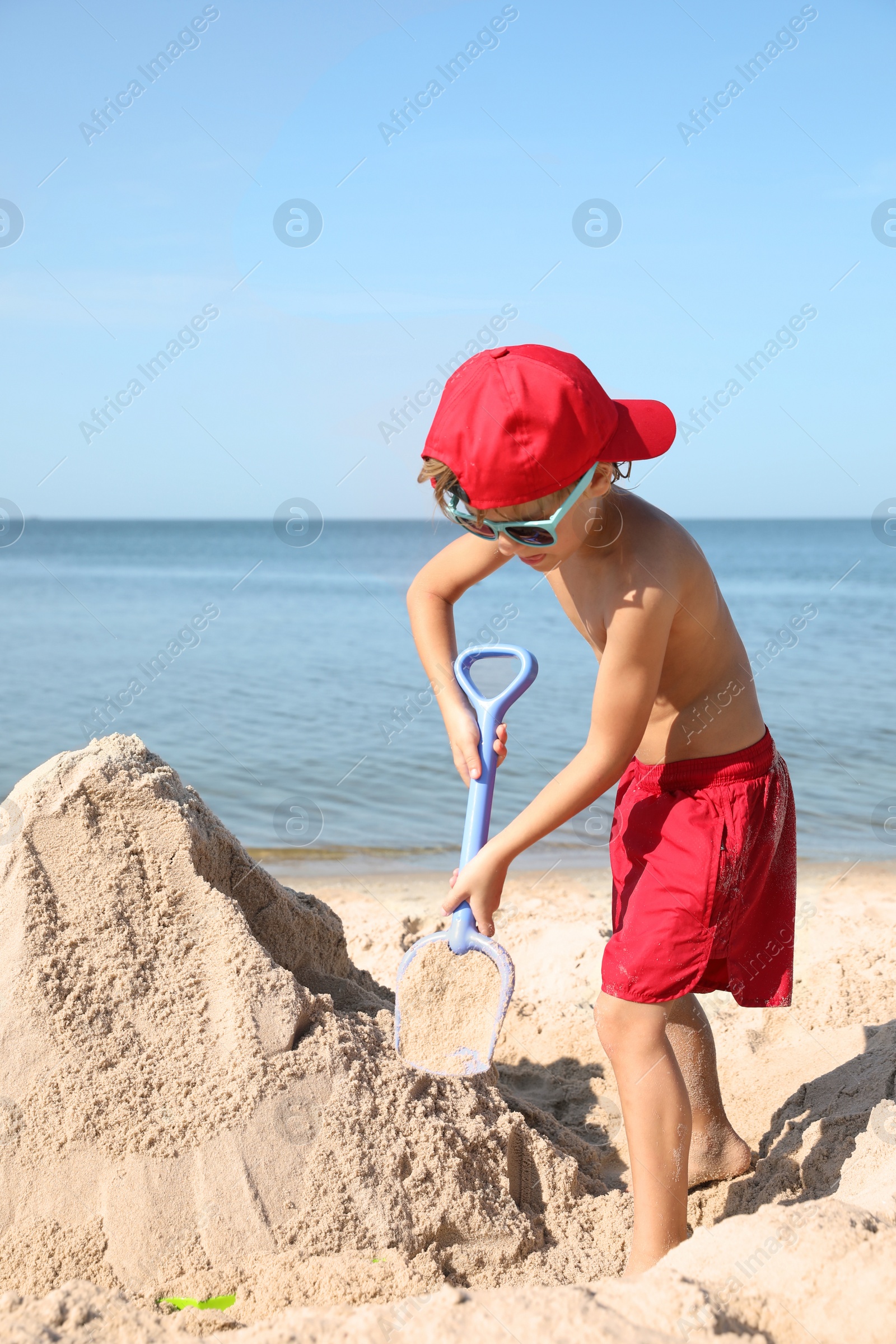 Photo of Cute little child playing with plastic shovel at sandy beach on sunny day