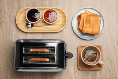 Toaster, roasted bread, jams and coffee on wooden table, flat lay