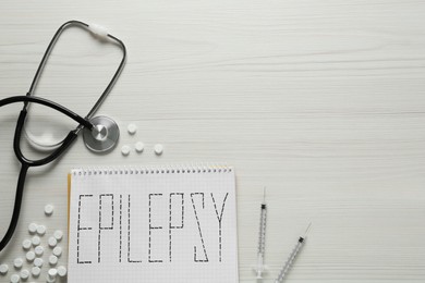 Photo of Notebook with word Epilepsy, stethoscope, pills and syringes on white wooden table, flat lay. Space for text