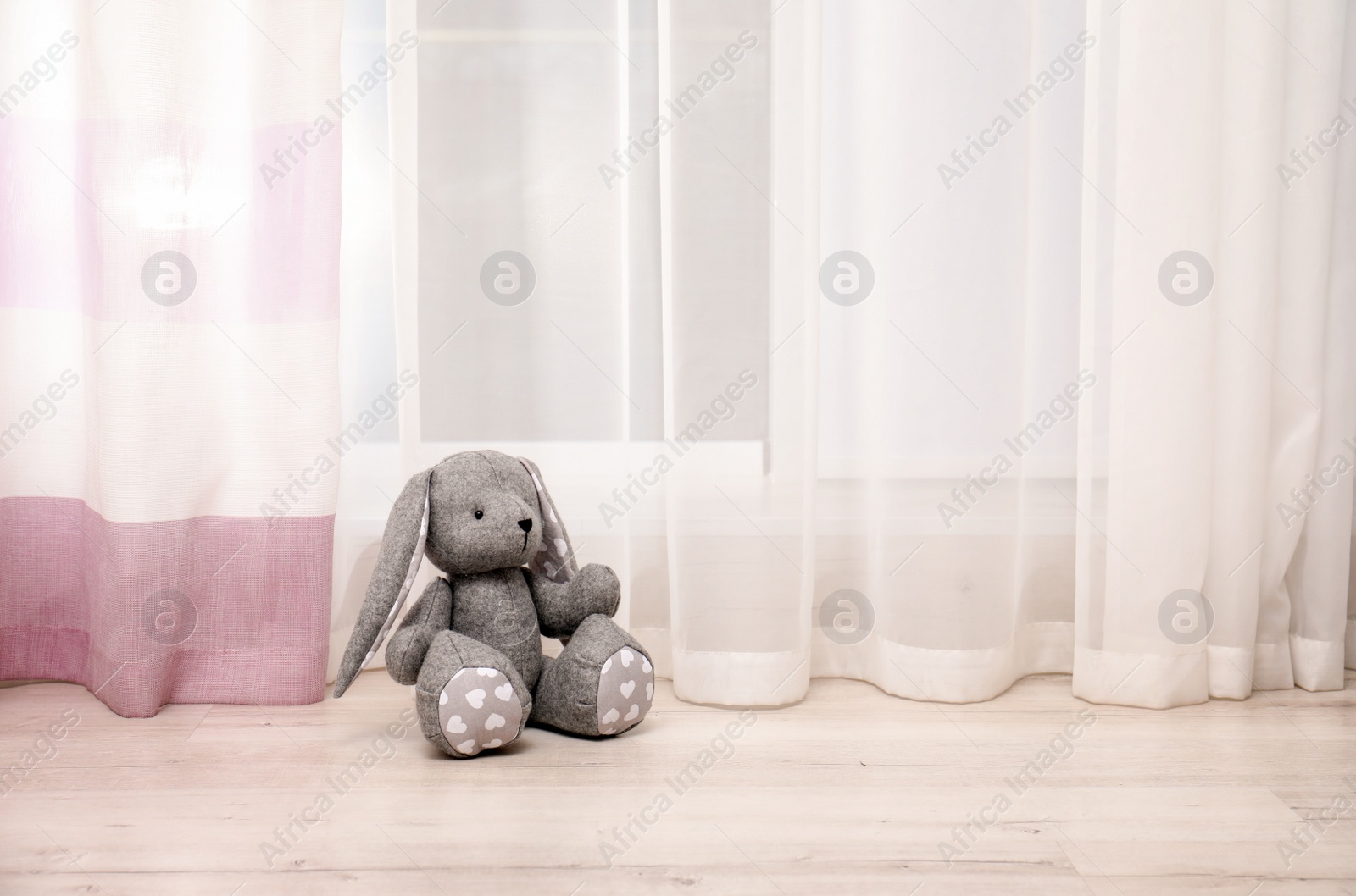 Photo of Toy rabbit on floor near window in child room. Space for text