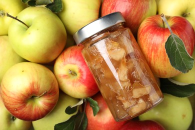 Photo of Delicious apple jam in jar on fresh fruits, top view